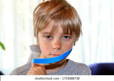 Boy Removes Blue Duct Tape From His Face. Child Mouth Is Taped Shut. The Concept Of Kid Wants To Talk.