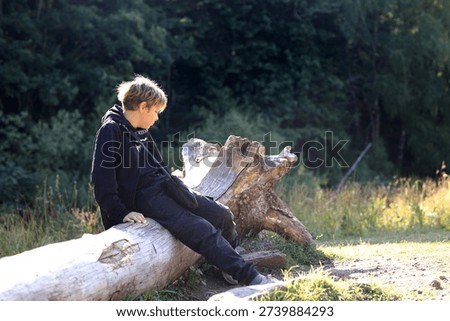 Boy resting on a fallen tree trunk during a hike. Teberda Nature Reserve excursion concept. Outdoor adventure for children.