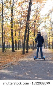 Boy Rides A Hoverboard In The Autumn Park In Sunny Day. Teenager Alone In The Fall Forest. Guy On Blue Gyro Board. Loneliness Concept