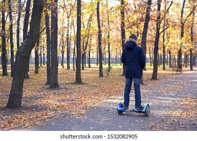 Boy Rides A Hoverboard In The Autumn Park. Teenager Alone In The Fall Forest. Guy On Blue Gyro Board. Loneliness Concept