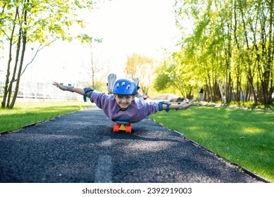a boy rides on a skateboard lying on his stomach, a child in a purple helmet and protection on his arms and legs lies on a city cruiser in a skate park