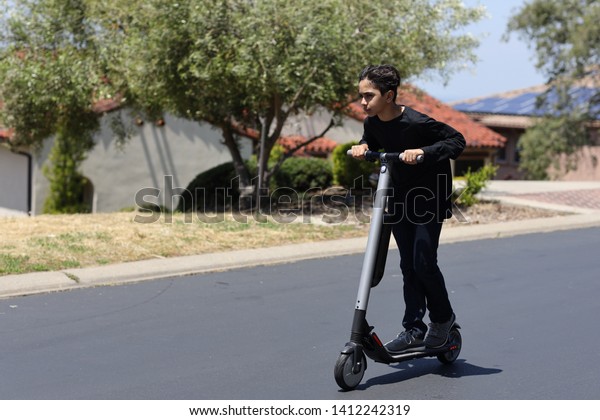 Boy\
riding with his electric scooter on a sunny\
day.