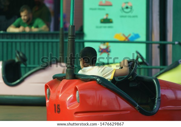 Boy riding on the bumper car / dodgems. \
Flat ride which draw power from the floor and ceiling and which are\
turned on and off remotely by an operator.\
