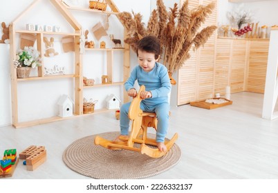 un niño montando un juguete de caballo de madera en un dormitorio blanco con decoración. Un niño está jugando en la guardería. Juguetes para niños. el interior infantil.