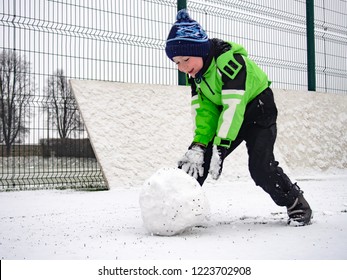 Boy Rolling Snowball On Playground