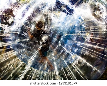 Boy Running Away Inside A Giant Plastic Ball That Is Refracting Light Into All The Colors.