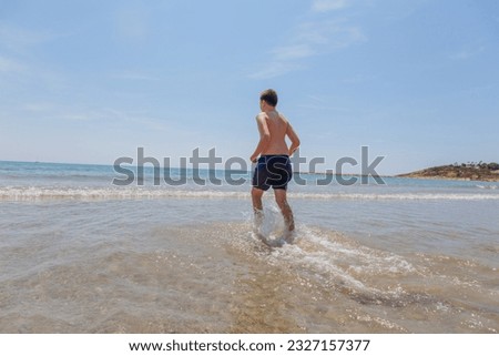 boy runs along the coast near the wavy sea on a sunny summer day. A cute child runs along the summer sea.