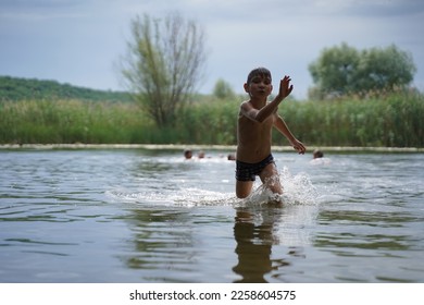 The boy runs out of the water. Portrait of a child merrily running from the water to the shore in splashes. Selective focus - Shutterstock ID 2258604575