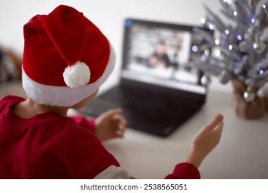 Boy in Santa Hat Video Calling Next to Laptop and Small Christmas Tree - Powered by Shutterstock