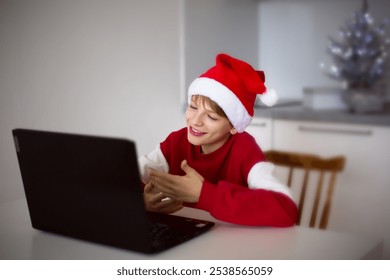 Boy in Santa Hat Video Calling Next to Laptop and Small Christmas Tree - Powered by Shutterstock