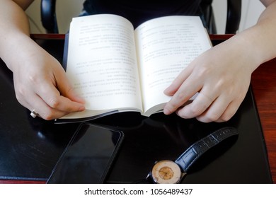 The boy sat at the table, reading with a book in his hand.