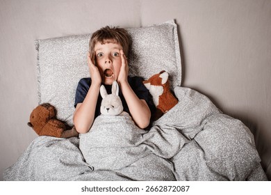 The boy was scared before going to bed. Night terrors in a child. The kid covers his face with his hands in a fear. Children's experiences. Boy in the bed. View from above. Sad psychological state.