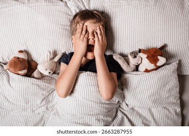 The boy was scared before going to bed. Night terrors in a child. The kid covers his face with his hands in a fear. Children's experiences. Boy in the bed. Air alarm. Sad psychological state.