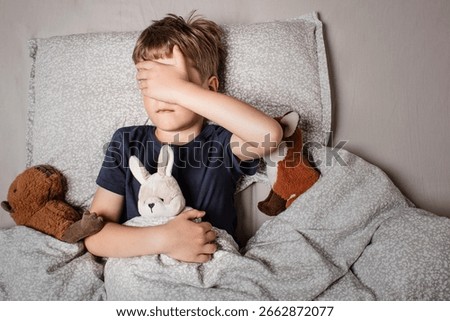 The boy was scared before going to bed. Night terrors in a child. The kid covers his face with his hands in a fear. Children's experiences. Boy in the bed. View from above. Sad psychological state.
