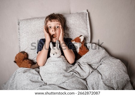 The boy was scared before going to bed. Night terrors in a child. The kid covers his face with his hands in a fear. Children's experiences. Boy in the bed. View from above. Sad psychological state.