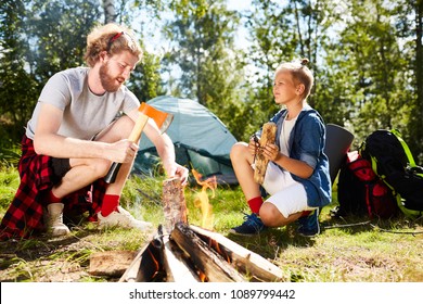 Boy Scout Helping His Father With Preparing Firewood For Campfire On Summer Weekend