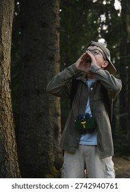 Boy shouting loudly in a forest while wearing binoculars and backpack, potentially lost or calling for help
