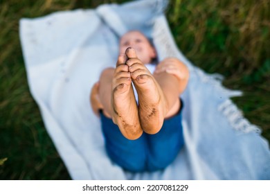 The boy shows his dirty feet lying on the ground with grass - Shutterstock ID 2207081229