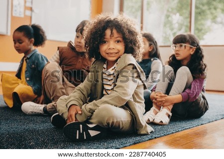 Boy sits in an elementary school class, he is looking at the camera. Multiracial kid attends a co-ed primary school with a group of multiethnic children. Foto stock © 
