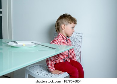 Boy Sits In The Kitchen And Refuses To Eat. Child Does Not Want To Eat Food And Turns Away From Food. 