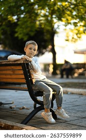 A boy sits on a bench in a quiet town on a warm day. A peaceful moment in the heart of a small town, enjoying the calm atmosphere and simple pleasures of childhood