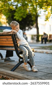 A boy sits on a bench in a quiet town on a warm day. A peaceful moment in the heart of a small town, enjoying the calm atmosphere and simple pleasures of childhood