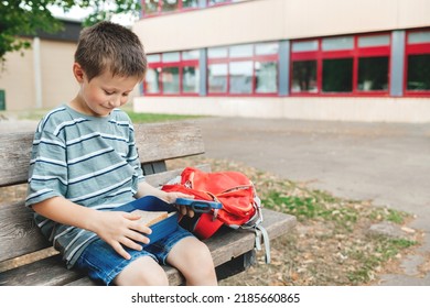 The boy sits on a bench in the school yard and takes out a sandwich from the lunch box for a snack. Nutrition for children while studying