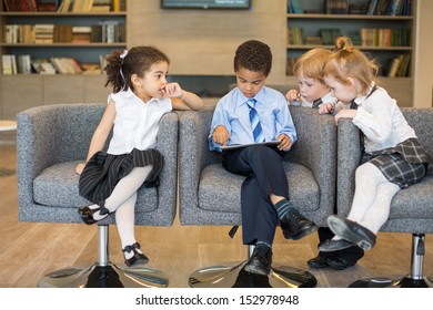 Boy sits on a chair and using a tablet, but the other kids look up to him