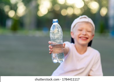 A Boy Sits On A Green Lawn On A Football Field And Holds A Bottle Of Water. Focus On The Water Bottle.