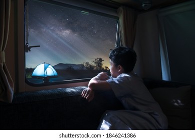 A boy sitting by the window of a van alone Look at the stars and the milky way Camping a tent in winter with family. Long exprosure with grain.