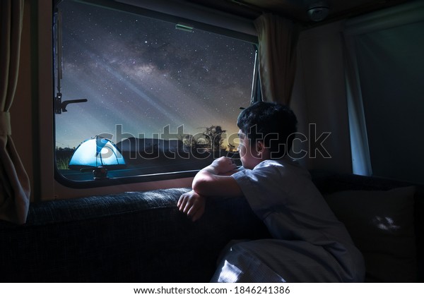 A boy sitting by the window of a van alone Look at\
the stars and the milky way Camping a tent in winter with family.\
Long exprosure with grain.