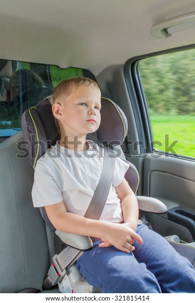 Boy\
sitting in a car in safety chair fasten by seat\
belt