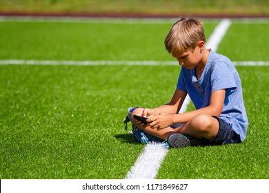 Boy sitting with cell phone sitting in empty football stadium field and looking video, typing, playing - Powered by Shutterstock