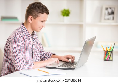 Boy sitting at desk with laptop and doing homework. Side view.