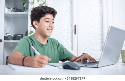 
A boy is sitting at a desk with a laptop and a pen with which he writes in his notebook. He smiles and is happy. - Powered by Shutterstock