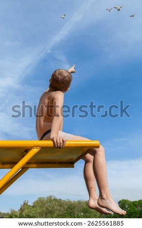 Boy sitting on bench pointing at airplane in sky. Concept of wonder and dream of flying
