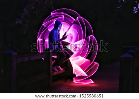 Boy sitting on a bridge with his smartphone in his hand. Violet light effect with a light saber in lightpainting