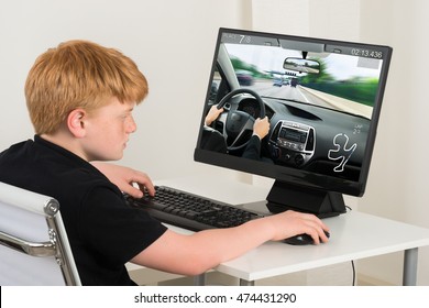 Boy Sitting On Chair Playing Car Game On Computer At Home