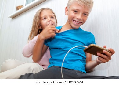 Boy Is Sitting On Floor And Watching Videos On Phone. Kid Does Not Share Phone With Girl. Sister Reaches Out To Take Away Phone And Also Play Mobile Games