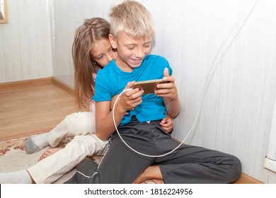 Boy Is Sitting On Floor And Watching Videos On Phone. Kid Does Not Share Phone With Girl. Sister Reaches Out To Take Away Phone And Also Play Mobile Games