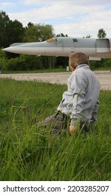 
A Boy Is Sitting On The Green Grass Near The Runway Of A Military Airfield Against The Background Of A Strategic Bomber
