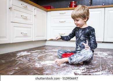 A boy sitting on the kitchen floor and playing with flour. 