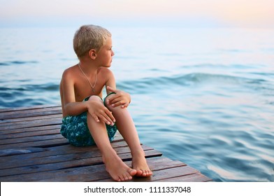 Boy, Sitting On A Wooden Jetty At Sea Beach