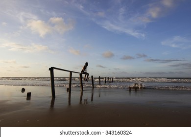 A boy sitting over the old fence in the beach during sunset.