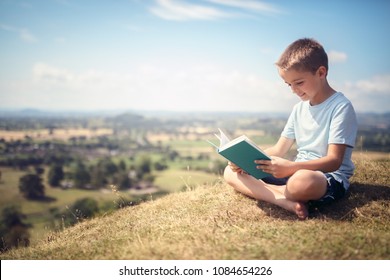 Boy sitting and relaxing on a hill reading a book in a meadow concept for education and relaxing