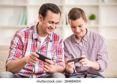 Boy sitting at sofa with his father and using phone.