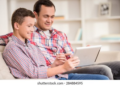 Boy sitting at sofa at home with father and using laptop. - Powered by Shutterstock