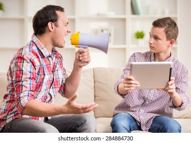 Boy sitting at sofa and using digital tablet while his father shouting to him.