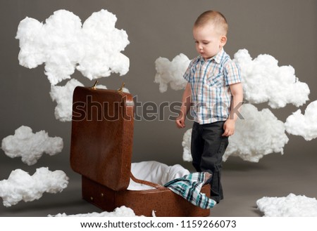 the boy is sitting in a suitcase and going on a journey, clouds of cotton wool as a decoration, gray background