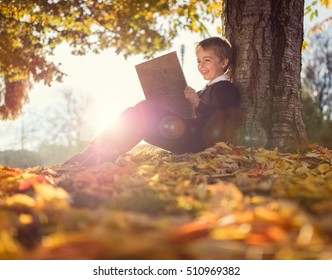 Boy sitting under a tree reading a book in an autumn sunset concept for education and nature